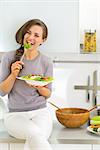 Happy young woman eating greek salad in modern kitchen