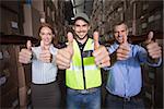 Warehouse team smiling at camera showing thumbs up in a large warehouse