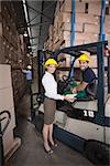 Warehouse manager smiling at camera with forklift driver in a large warehouse