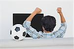 Rear view of a soccer fan cheering while watching tv
