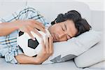 Football fan sleeping on couch hugging ball