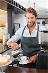 Barista pouring milk into cup of coffee at the coffee shop