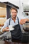 Handsome barista offering a cup of coffee to camera at the coffee shop