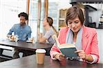 Pretty brunette enjoying her coffee with a book at the coffee shop