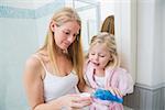 Happy woman pouring blue mouthwash with daughter at home in the bathroom