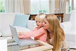 Cute daughter and mother using laptop on coffee table at home in the living room