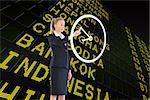 Composite image of businesswoman pointing to a white clock against black airport departures board for asia