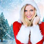 Pretty girl smiling in santa outfit against snowy landscape with fir trees