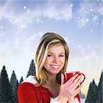 Pretty santa girl holding mug against snowy landscape with fir trees