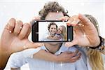 Hand holding smartphone showing man piggybacking woman at beach