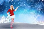 Pretty girl presenting in santa outfit against snowy landscape with fir trees