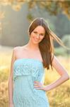 Portrait of young woman standing in a meadow at sunset in early autumn, looking at camera and smiling, Bavaria, Gremany