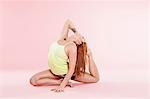 Studio shot of young woman in yoga position bending backwards on floor touching toes