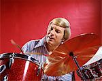 1960s 1970s BLONDE MAN STRIPED SHIRT RED BACKGROUND PLAYING DRUMS DRUM DRUMMING CYMBAL PERCUSSION MUSIC MUSICIAN RHYTHM