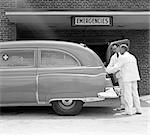 1950s TWO AMBULANCE DRIVERS EMTS DOCTORS AT REAR OF AMBULANCE AT HOSPITAL EMERGENCY ROOM ENTRANCE