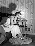 1950s LATE NIGHT SERIOUS UPSET SLEEPLESS WOMAN SITTING ON EDGE BED LOOKING AT CAMERA INSOMNIA ANGRY SICK WORRY STRESSED WORRIED