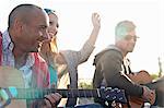 Three adult friends playing acoustic guitars on Bournemouth beach, Dorset, UK