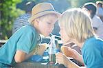 Two young boys drinking from bottle with straws