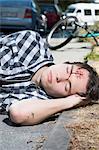 Young man lying on roadside with bleeding forehead