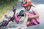 Young girl with injured leg sitting on road with bicycle