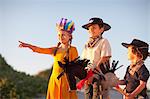 Three children dressed as native american and cowboys pointing from sand dunes