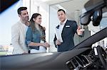 Mid adult couple and salesman chatting in car dealership