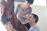 Young female horseback rider with instructor in indoor paddock