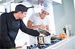 Two male chefs cooking on hob in commercial kitchen