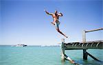 Couple jumping off wooden dock into water