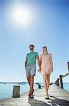 Couple holding hands walking along wooden dock