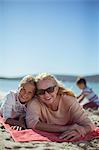Grandmother and granddaughter laying on beach towel together