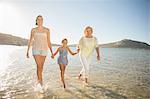 Three generations of women walking in waves