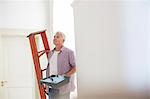 Older man carrying ladder and paint tray