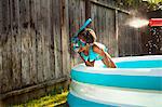 Girl in scuba mask getting sprayed with water gun in garden paddling pool