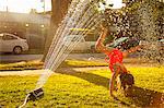 Girl doing handstand under in garden sprinkler