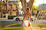 Girl with beachball in garden sprinkler