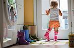 Female toddler wearing rubber boots looking out of back door window