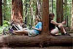 Two mid adult women looking down at smartphone and digital tablet in forest