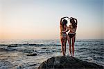 Two young women standing on rock in ocean, rear view