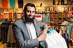 Portrait of tailor leaning against rails in men's clothes shop