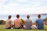 Rear view of four friends sitting looking away to sea