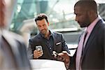 A group of three businessmen, two checking their phones.