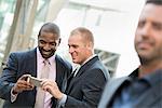 Two businessmen checking a phone and laughing, one man in the fore.