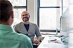 Two men seated in a light airy office environment, talking.