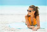 Smiling young woman in sunglasses laying on sea coast looking on copy space