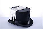 Black top hat with silk white gloves, studio shot on white background with reflection