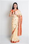 Asian Indian girl in a greeting pose, traditional sari costume, full length standing on plain background