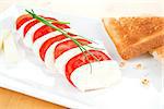 Mozzarella and tomato with toast bread on white plate decorated with fresh chive.