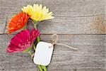 Three colorful gerbera flowers with tag on wooden table