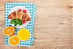 Orange juice and fresh croissant with berries on wooden table background with copy space